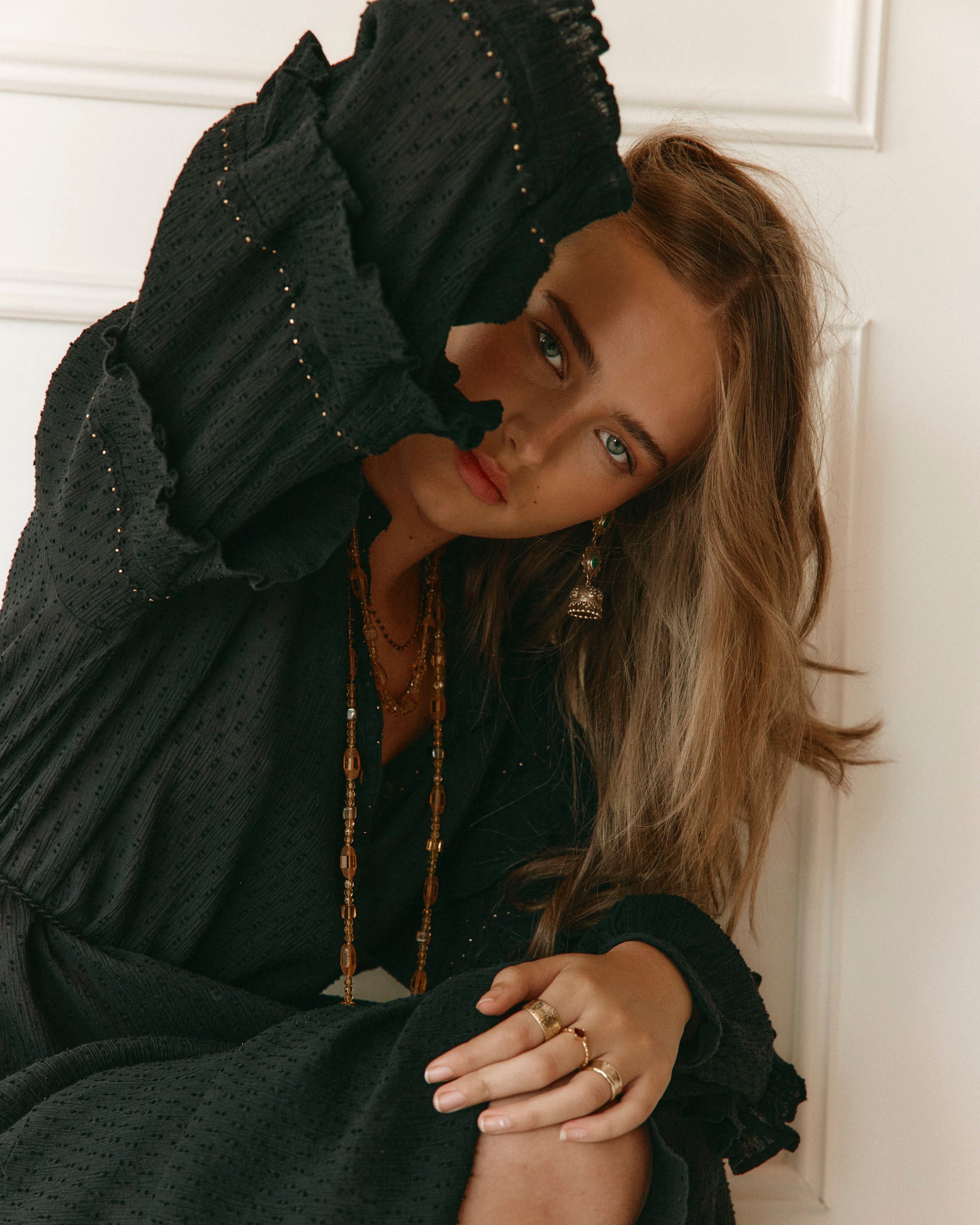 LAKOÈN model wears our Anais Dress in black gotton dobby with delicate gold hand beading edging the sleeve frills, and tonal hand embroidery Our Brass Freya Emerald drops peak through her hair - hand-crafted - slow luxury - bohemian - everyday elegance