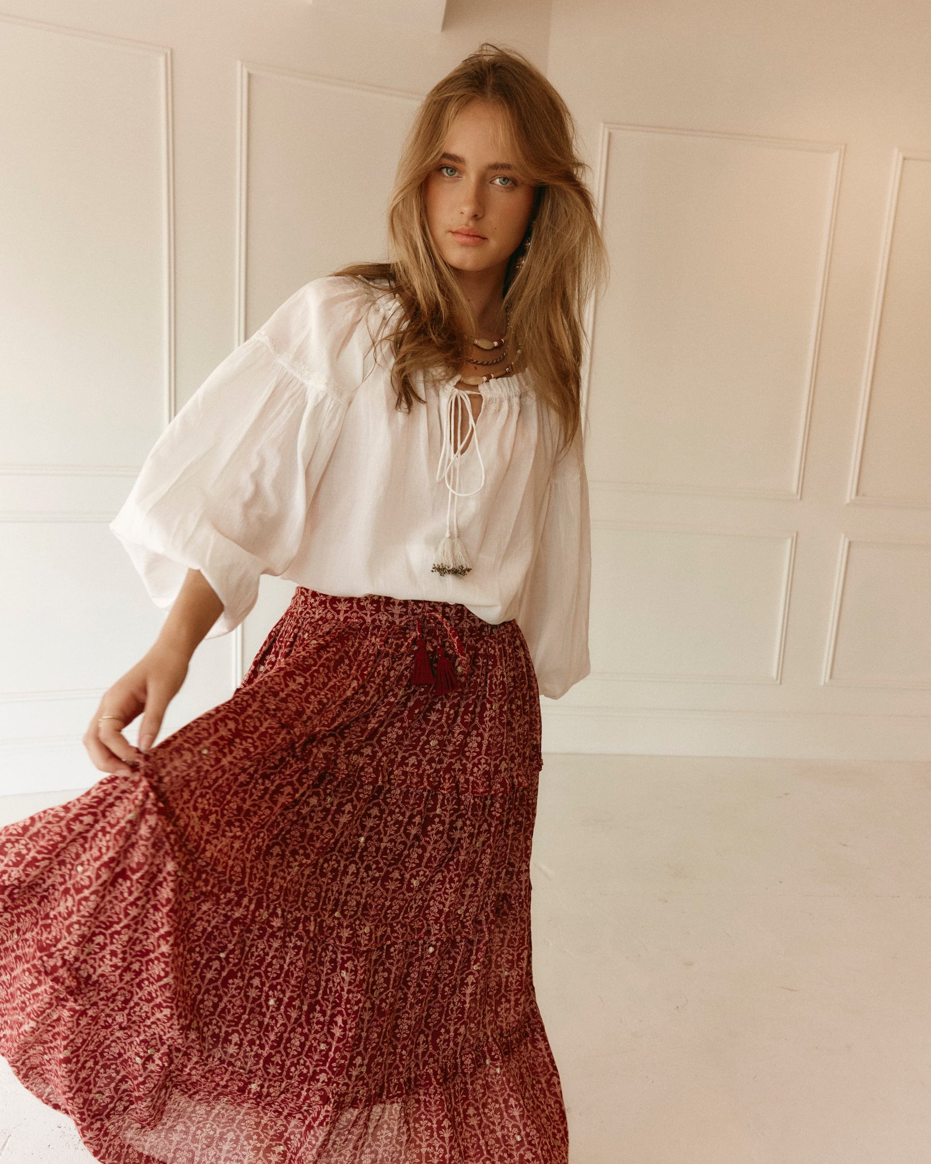 LAKOÈN model twirls in our tiered Emile Maxi Skirt. Crafted from fine cotton with a delicate block-inspired print in rose and rich burgundy hues, adorned with shimmering gold embroidered dots. Pictured with our White Emory blouse - slow-luxury - hand-crafted - bohemian - ethically-made