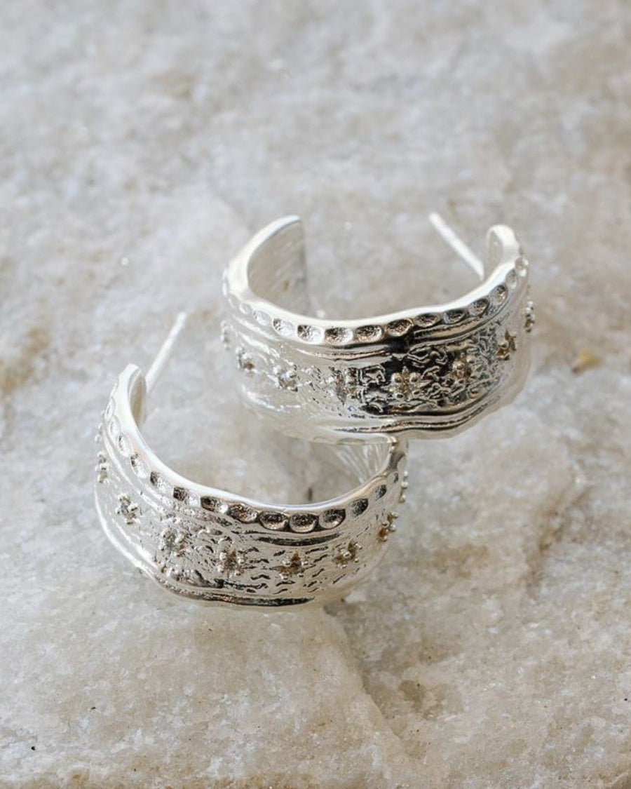 Pair of silve LALKOEN Inca hoop earrings on a marble surface
