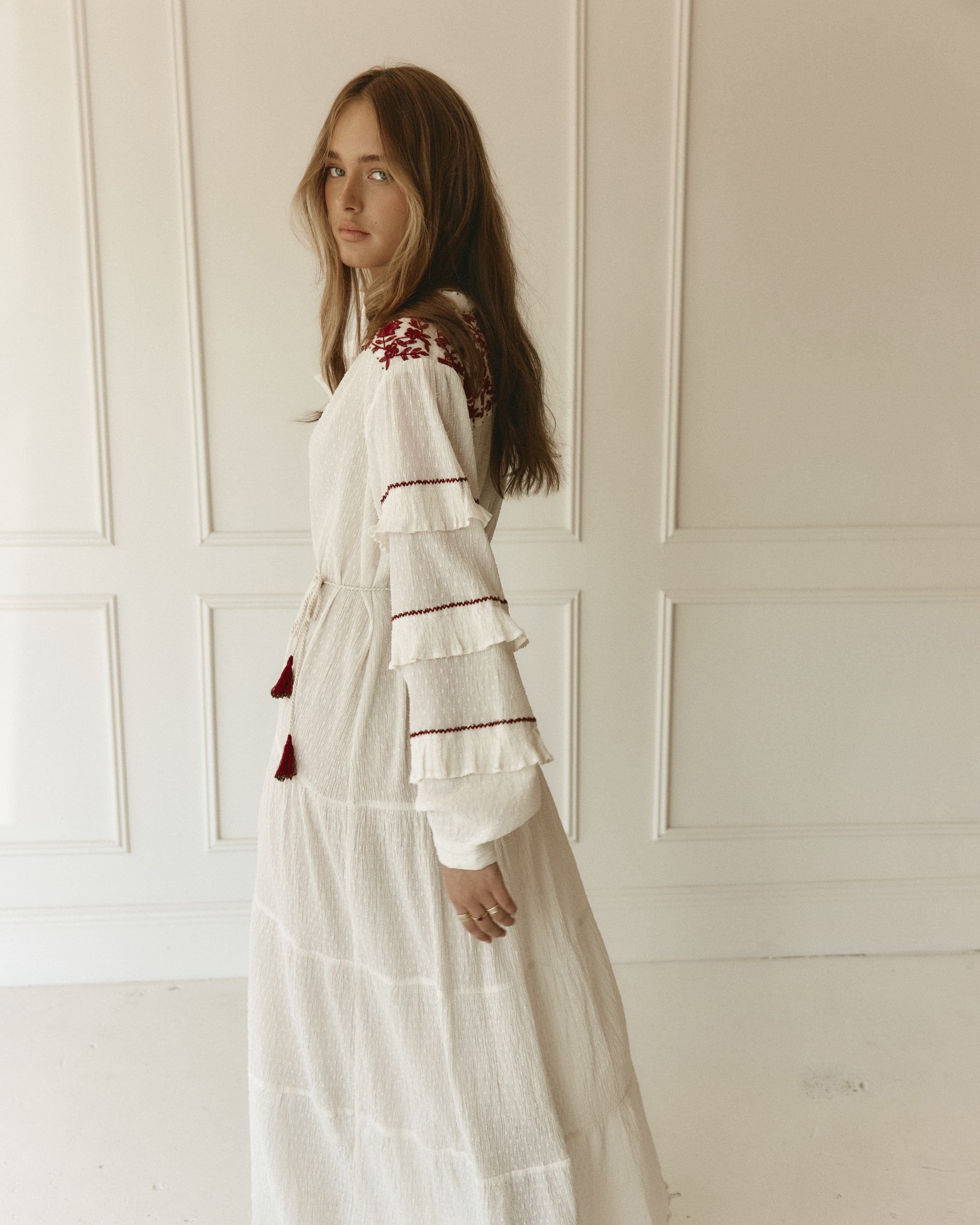 Lakoen Anais Dress in white cotton dobby with floral embroidery in burgundy and frilled bishop sleeves