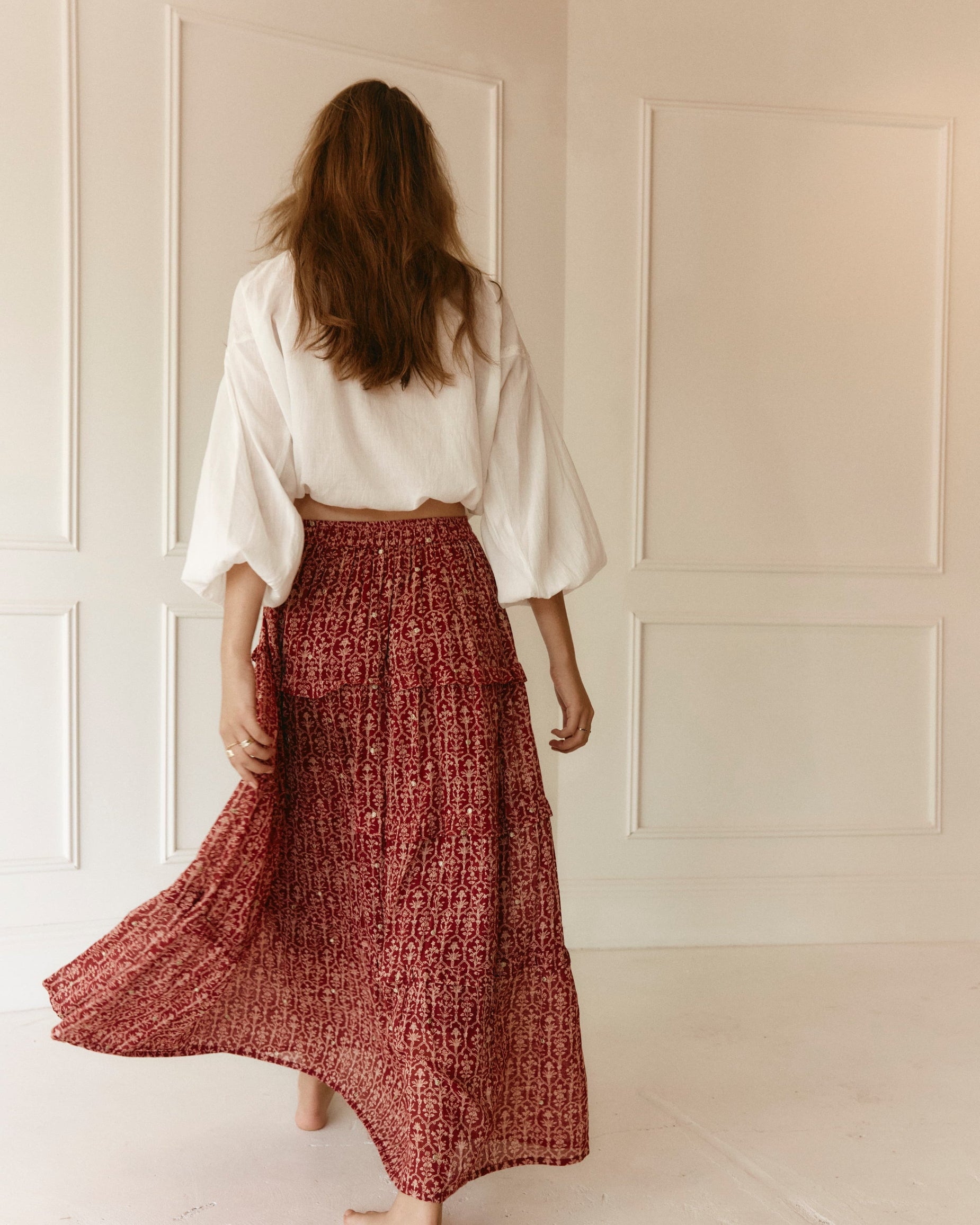 LAKOÈN model walks in our tiered Emile Maxi Skirt. Crafted from fine cotton with a delicate block-inspired print in rose and rich burgundy hues, adorned with shimmering gold embroidered dots. Pictured with our White Emory blouse - slow-luxury - hand-crafted - bohemian - ethically-made