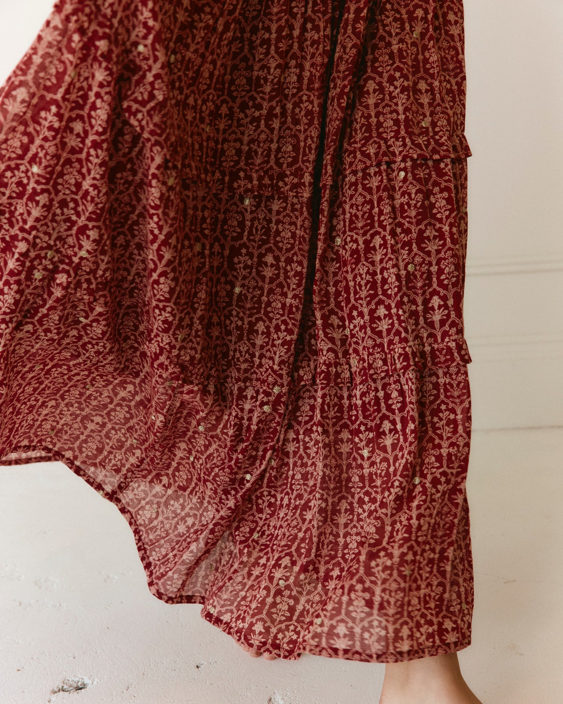 Close-up of LAKOÈN model stepping in our tiered Emile Maxi Skirt. Crafted from fine cotton with a delicate block-inspired print in rose and rich burgundy hues, adorned with shimmering gold embroidered dots.  - slow-luxury - hand-crafted - bohemian - ethically-made